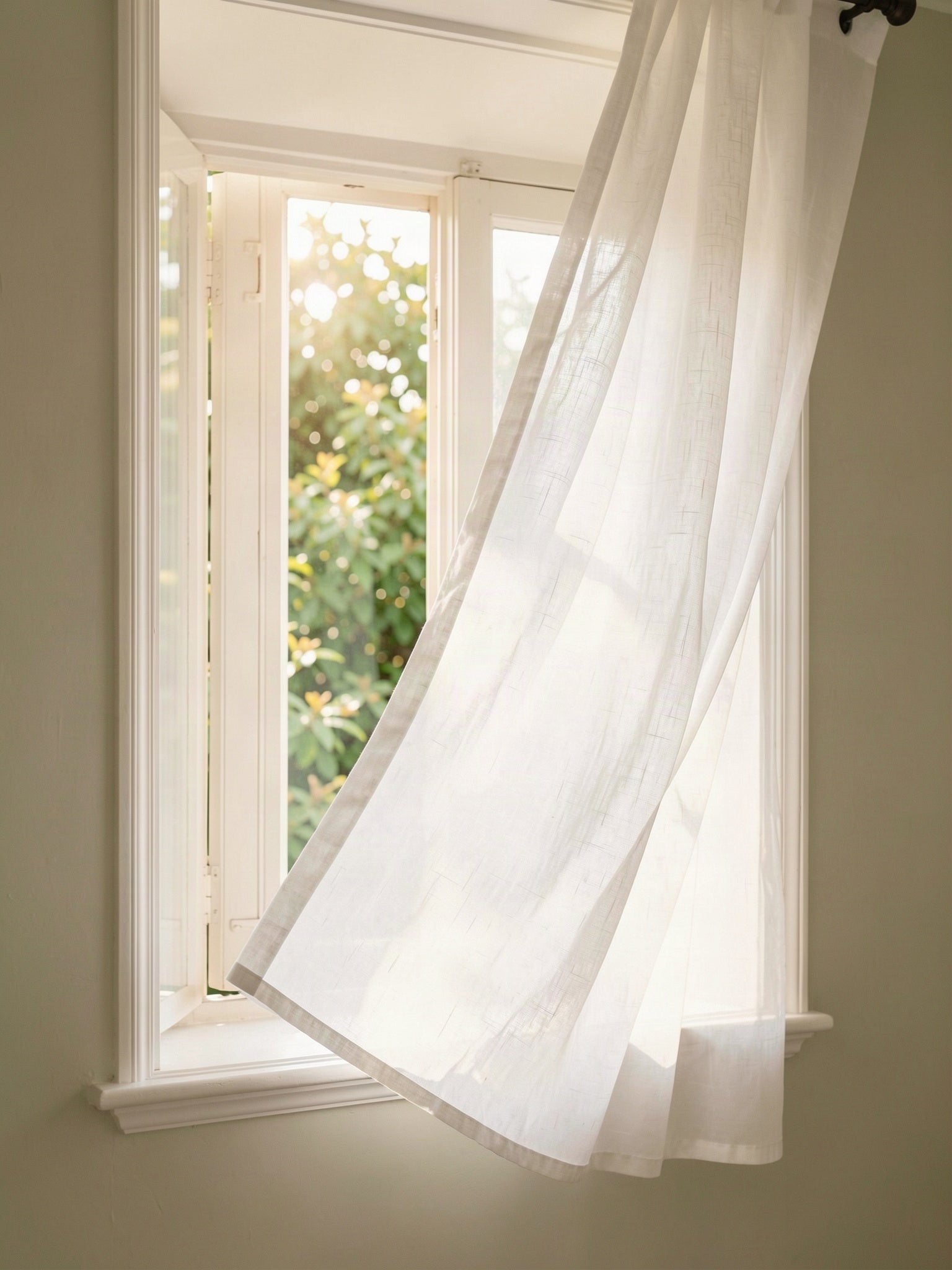 Offenes Fenster mit wehendem Leinenvorhang im Morgenlicht